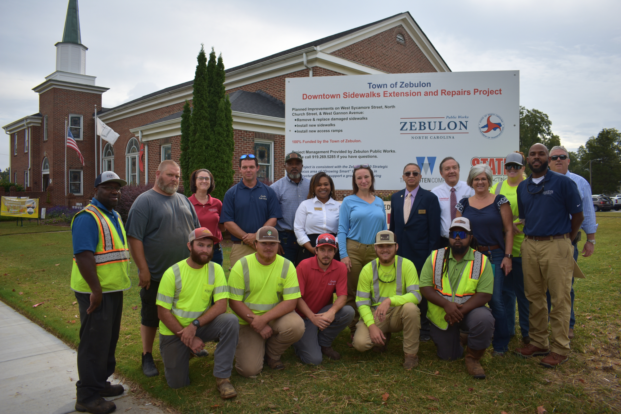 Zebulon employees gather around a sign for "Downtown Sidewalk Extension and Repairs Project"