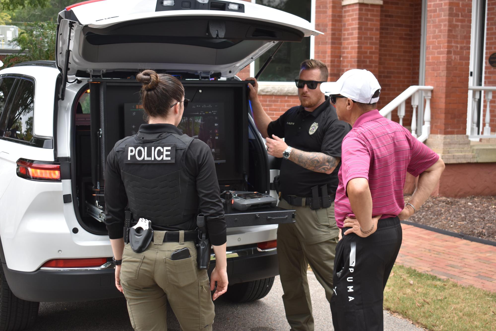 Two ZPD officers speaking to a man at the back of a ZPD vehicle.