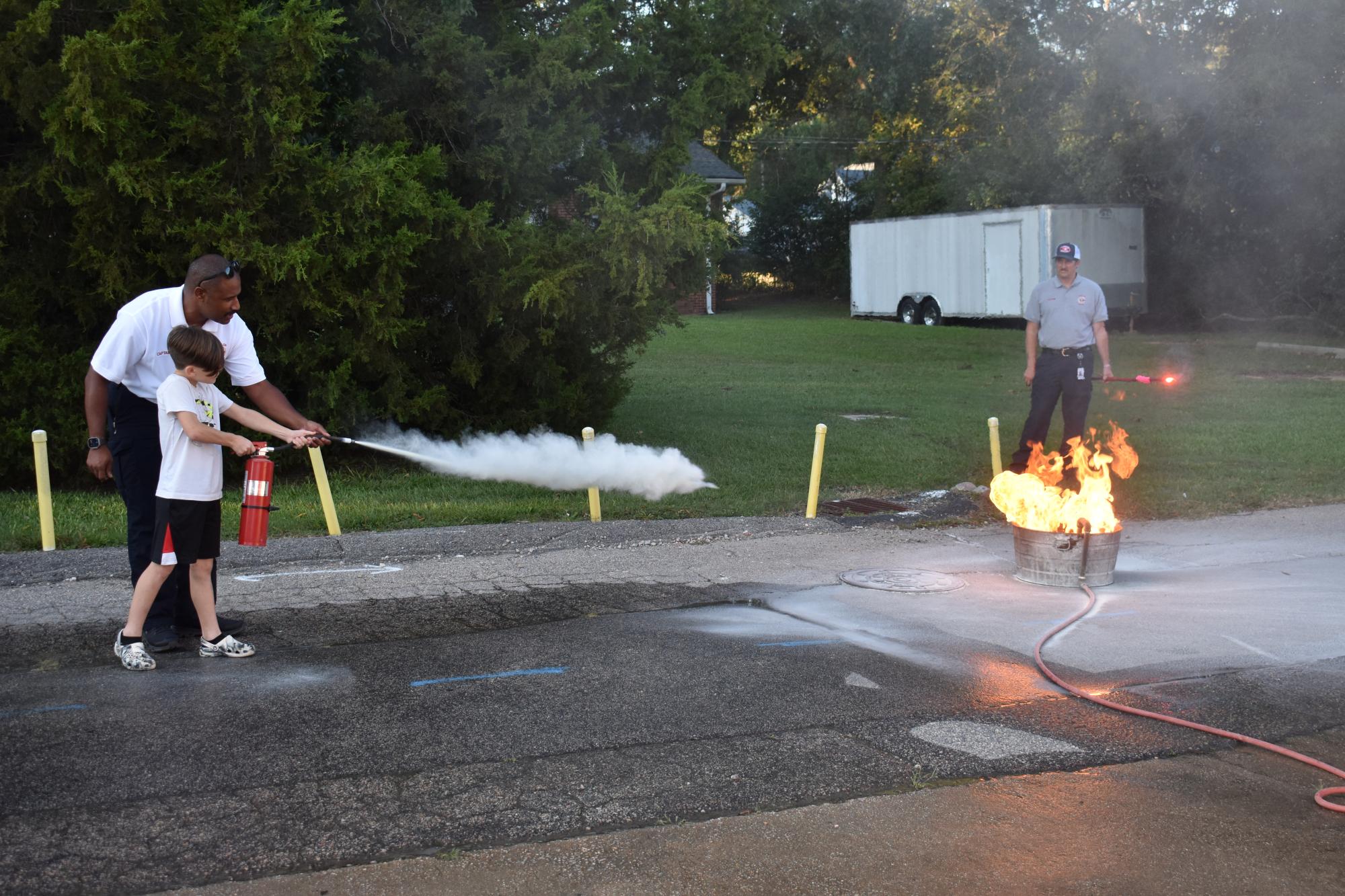 A ZFD firefighter helping a child work a fire extinguisher to put out a controlled fire.